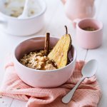 Een lichtroos ontbijtkommetje staat op tafel, met hierin de kruidige chai porridge met een halve peer en een kaneelstokje. Er is ook een roze theepot met bijpassend kopje.