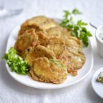 Krokante courgetteplakjes liggen op een bordje, afgewerkt met enkele blaadjes peterselie. De aioli staat langs het bordje.