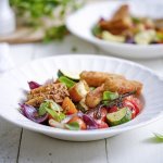 Een heerlijk en rijkgevuld slaatje is geserveerd in een diep wit bord. De kleurtjes van de basilicum, tomaten, rode ui en courgette zijn uitgesproken en zien er fantastisch uit. Dit gerecht geeft je een boost. 