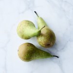 Drie peren liggen op een marmere aanrecht. De kleuren van de conference peren zijn groen en komen mooi uit op het werkblad van witte marmer.