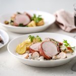 Op tafel staan twee porties uitgeschept. Het heerlijk bereide varkenshaasje ligt op de romige champignonsaus met plakjes wortel. Er liggen ook ovengeroosterde aardappeltjes bij. Langs het bord ligt een servette, glaasje rode wijn en bestek. 