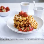 Op een bordje liggen enkele wafels met verse aardbeien en wat bloemsuiker. Er staat ook nog een tasje koffie langs. 