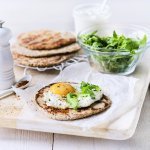 Het yoghurtbrood ligt op een houten snijplank. Hierop liggen meerdere ingrediënten om aan de slag mee te gaan, denk maar aan rucola, peper, extra yoghurt. 