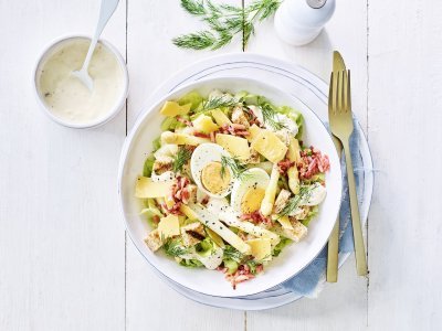 Een rijkgevulde salade staat klaar op tafel. Het witte bord is gevuld met sla, gekookte eitjes, stukjes asperges en kaasschilfers. Dat is de lente proeven in je bord, als je het mij vraagt!