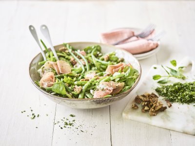 Een licht groene serveerkom is gevuld met onze groene salade boordevol, jawel, groene groenten. Denk maar aan verse sla, boontjes, paprika en erwten. De salade is afgewerkt met rozige gerookte hamsneetjes en verse groene kruiden.  