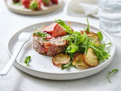 Zoek je een alternatief voor steak-tartaar? Wel dit is een zomerversie, nl eentje met kalfsvlees, aardbeien, tomaatjes en verse kruiden. We werkten het gerechtje af met gebakken aardappelplakjes en verse rucola. Er ligt een wit vork en servette naast om meteen aan te vallen. 