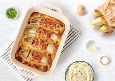 Gegratineerde witloofrolletjes opgerold in gekookte ham liggen mooi naast elkaar in een ovenschotel. De kaassaus is laat de rolletjes net bovenkomen. Er staat een pot heerlijke puree klaar om aan te vallen. 