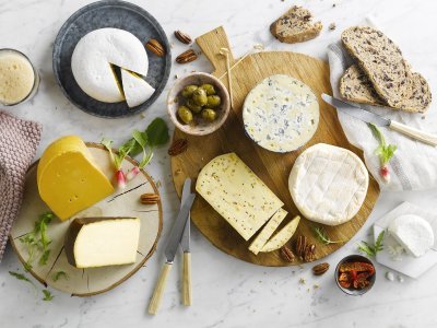 Kaasschotel op marmeren keukenblad. Verschillende Belgische kazen liggen op houten planken met brood, noten, radijzen en chutney erbij. 