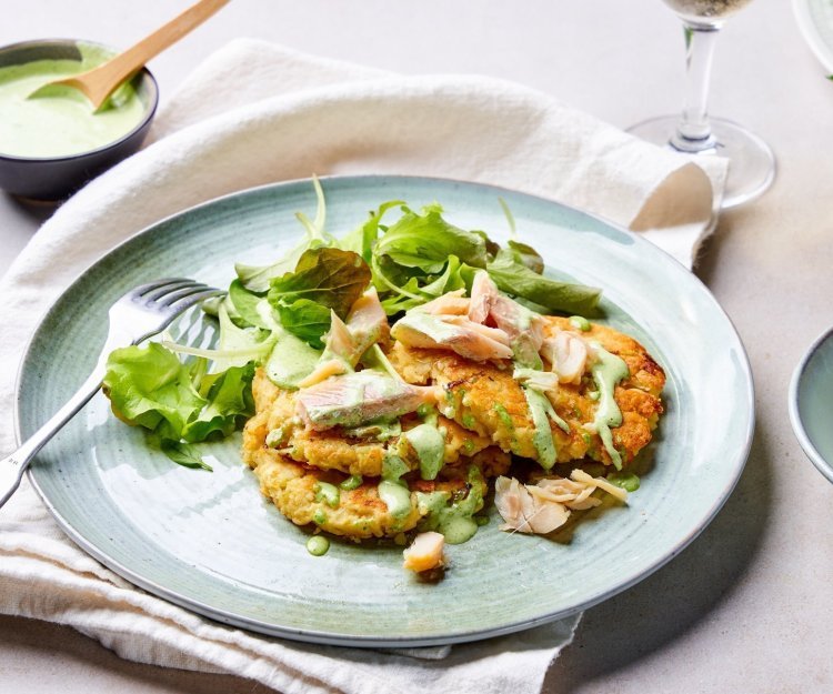 Op tafel staat een licht blauw bord, met hierop de goudgele pannekoekjes op basis van aardappelpuree. Het gerechtje is afgewerkt met enkele stukjes gerookte forel, sla en een groene dressing van verse kruiden. 