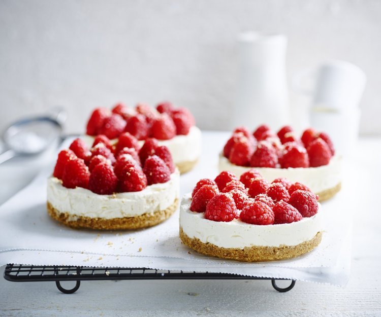 Wij maakten 4 kleine cheesecakes en staan op een wit boterpapiertje. Ze zijn afgewerkt met verse frambozen die een mooi contast geven met het witte van de kaas.