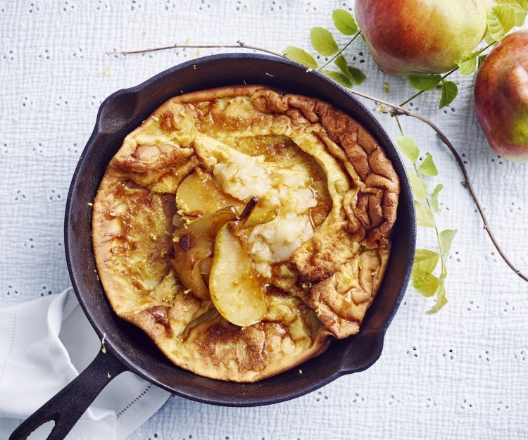 Een ovenpannenkoek met heerlijke peertjes, hij komt net uit de oven en ligt nog in de pan. Er liggen 2 verse peperen langs.