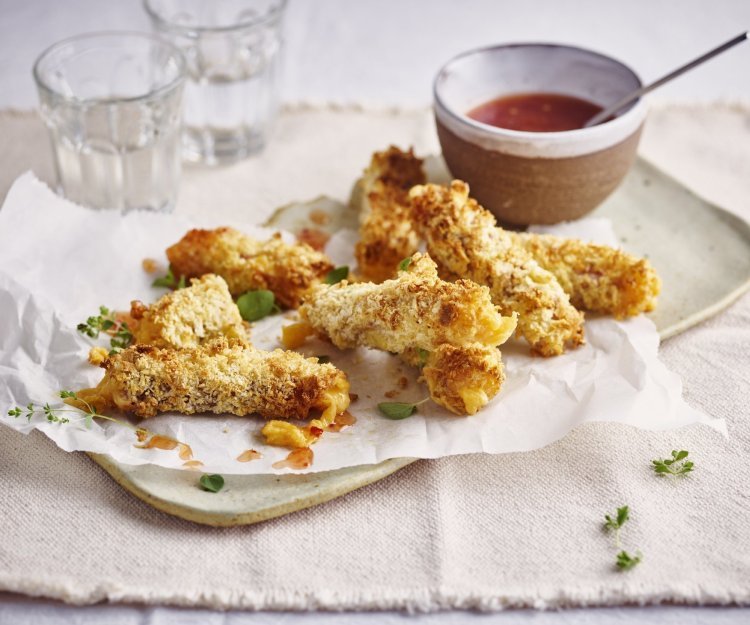 Krokante kaaskroketten liggen op een dienchaaltje, met een dipsausje in een zelfgedraaid keremakiekpotje. Er staan twee glaasjes water naast en de sticks zijn afgewerkt met verse oregano.