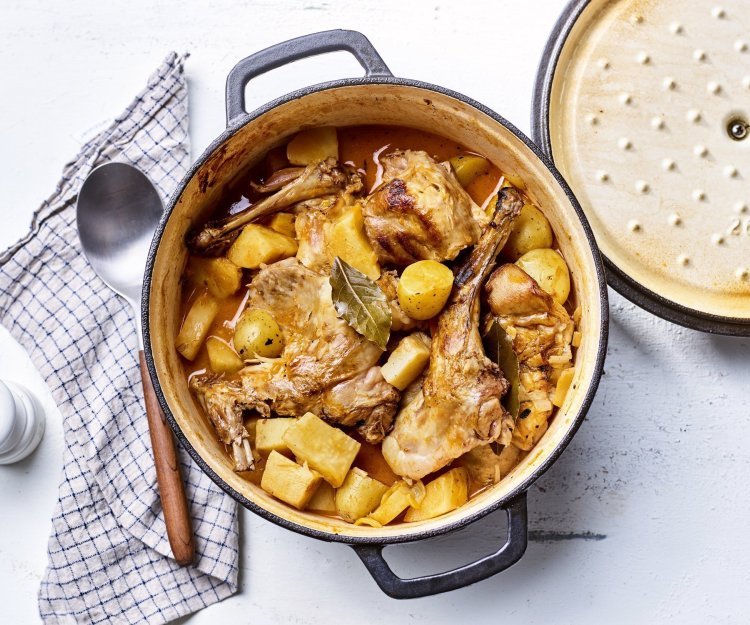 Op tafel staat een gietijzeren pot gevuld met de ragout van konijn. Hij heeft een gouden kleur door de pastinaak, wortel en krieltjes. 