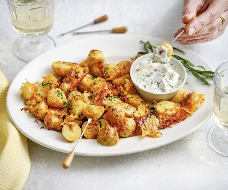 Een groot wit bord staat midden op de tafel, het is gevuld met heerlijke krokante aardappeltjes met kaas en een dipsausje van dragonmayonaise. Er is een hand die er eentje prikt en er staan twee glaasjes wijn. De aperitief is gestart. 