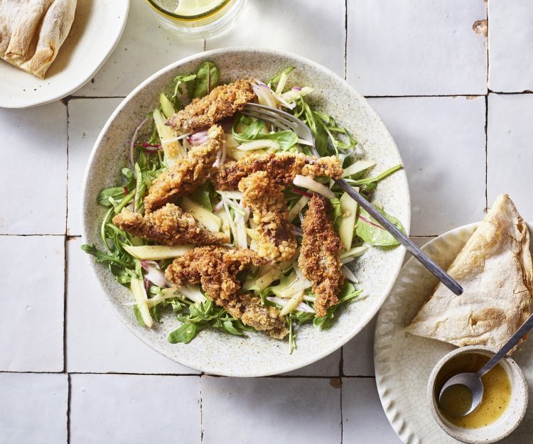 Er staat een diep bord op het aanrecht, gevuld met meerdere slasoorten en krokant gebakken leverreepjes. De mosterdressing staat er langs om zelf toe te voegen. 