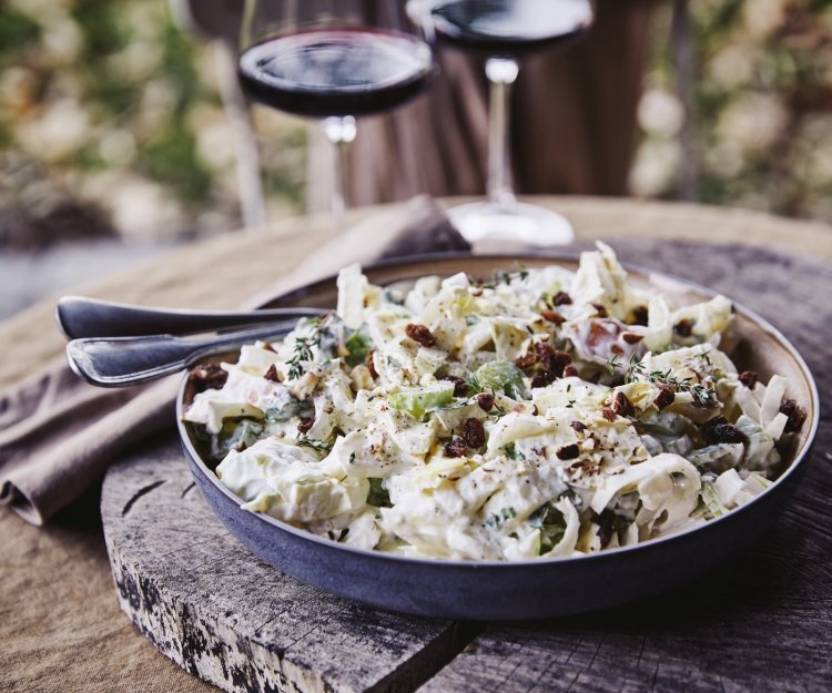 Een witloofsalade met yoghurtdressing, selder, rozijnen, appel en gember. Echt eentje om duimen en vingers van af te likken. De salade is geserveerd in een groot diep bord en staat op een boomstronkschijf.