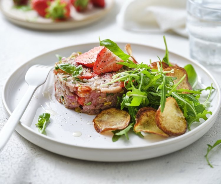 Zoek je een alternatief voor steak-tartaar? Wel dit is een zomerversie, nl eentje met kalfsvlees, aardbeien, tomaatjes en verse kruiden. We werkten het gerechtje af met gebakken aardappelplakjes en verse rucola. Er ligt een wit vork en servette naast om meteen aan te vallen. 