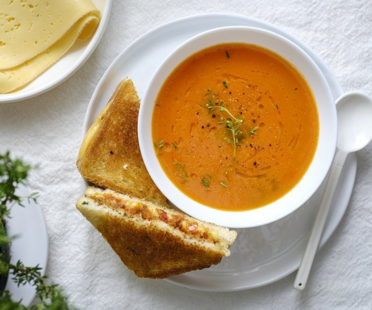 Een heerlijke kom soep staat klaar op tafel in een wit kommetje. Wij serveren hem met een toast van kaas en tomaatjes. Een heerlijke en voedzame lunch.