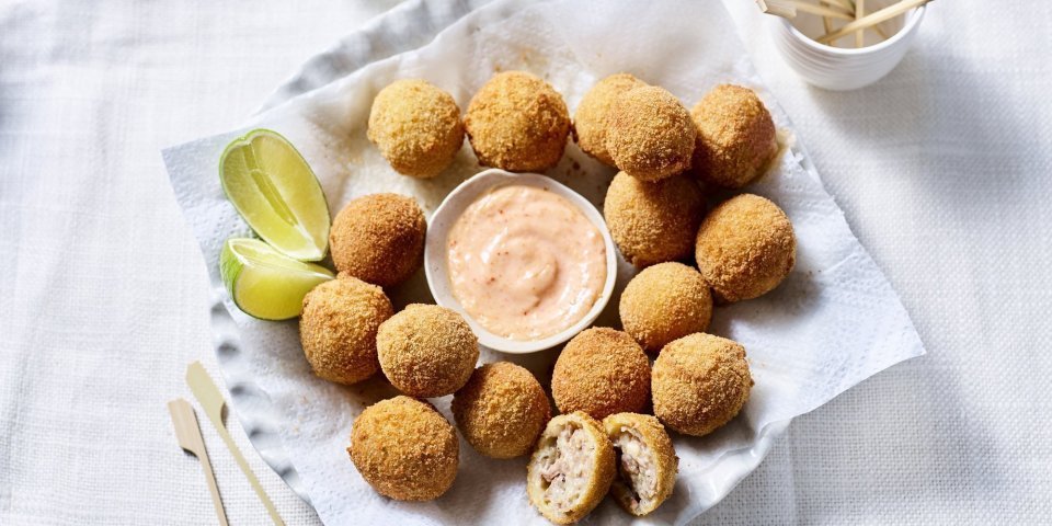 Bitterballen liggen te schitteren op een groot bord. In het midden staat een schaaltje met de pikante dipsaus en enkele partjes limoen. 