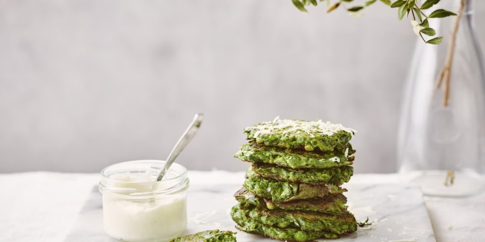 Enkele klaargemaakte fritters liggen gestapeld op een marmere snijplank. De fritters hebben een mooie groene kleur, er naast staat een glazen potje met de citroenmascarpone om te benuttigen als dip. 