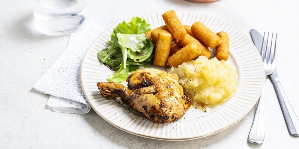 Op tafel staat een bord klaar met een gebraden kippenbout, goudgele appelmoes en kroketten. We serveren deze klassieker met nog wat extra sla en ev nog wat appelmoees. 