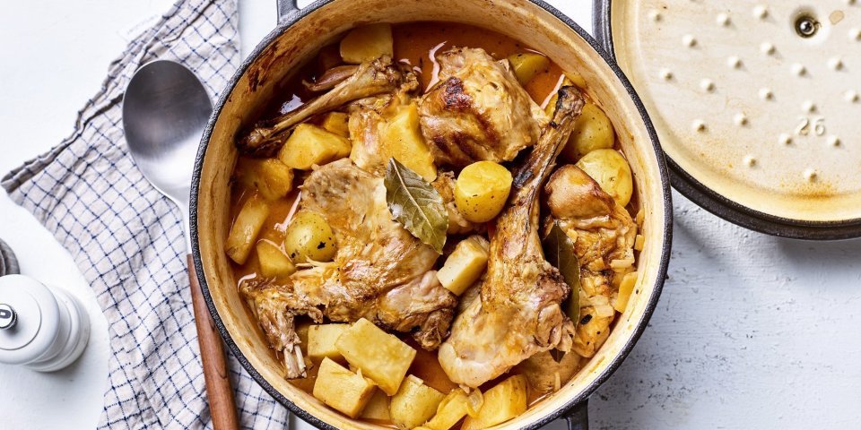 Op tafel staat een gietijzeren pot gevuld met de ragout van konijn. Hij heeft een gouden kleur door de pastinaak, wortel en krieltjes. 