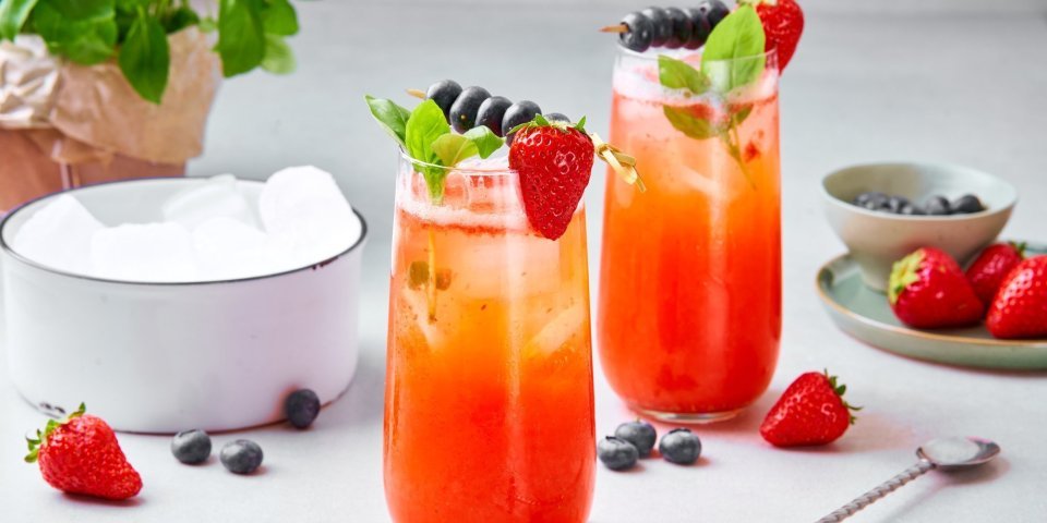 Twee mocktails staan op het aanrecht, klaar om te drinken. Hij heeft een mooie rode kleur door de aardbeien, het glaasje is afgewerkt met ijsblokjes, takje munt, aardbei aan het glas en een spiesje met blauwe bessen opgeprikt.