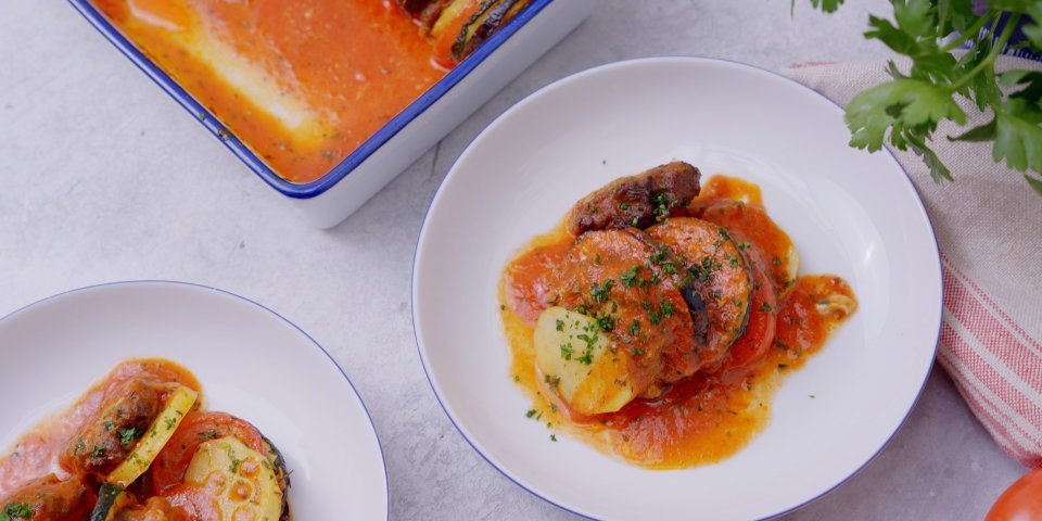 Twee bordjes staan op tafel met een uitgeschepte portie vanuit onze ovenschotel. We maakten een ovenschotel met plakjes groenten en schijfjes gehakt met tomatensaus.