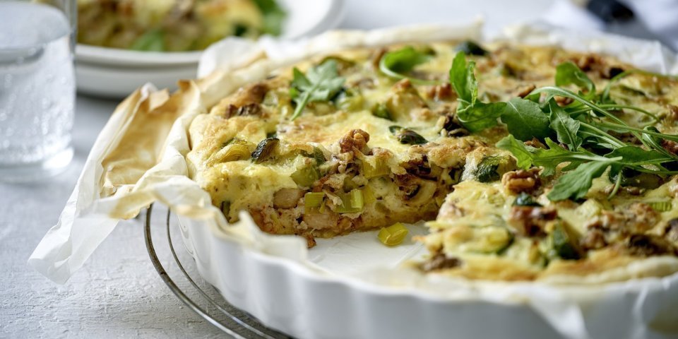 Een heerlijke quiche vers gebakken in een witte porseleinen taartvorm. Hij is gemaakt met spruitjes, champignons en prei. We voegden nog wat walnoten toe voor een extra bite. 