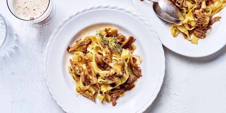 Op tafel staat een wit bord gevuld met tagliatelle en konijnenragout. Er staat een biertje langs, aangezien de ragout gemaakt is met Belgisch bier. 