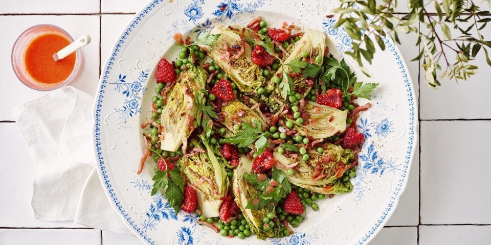 Een wit retro bordje staat op het aanrecht. Het is gevuld met een salade, gebakken spekjes en little gem. De frambozendressing is helder en roze, deze staat naast het bord in een glazen potje. 