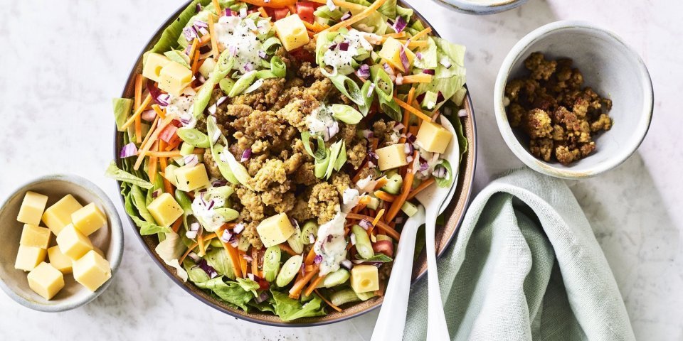 Een grote salade kom staat op het aanrecht, hij is gevuld met gemengde sla, komkommer, tomaten, worteltjes, stukjes kaas en gebakken gehakt. We werkte de salade af met een ranchdressing op basis van zure room en verse kruiden.