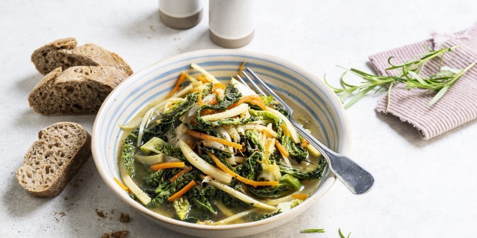 Op de tafel staat een portie uitgeschept van het vegetarische stoofpotje boordevol groenten. Denk maar aan witloof, savooikool, pastinaak en wortel. Wij serveren dit gerechtje met enkele sneetjes zuurdesembrood. 