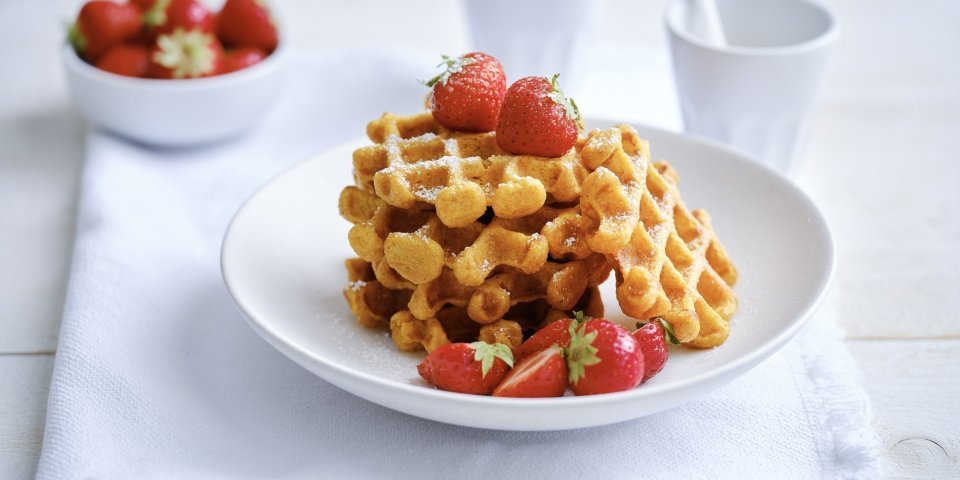 Op een bordje liggen enkele wafels met verse aardbeien en wat bloemsuiker. Er staat ook nog een tasje koffie langs. 