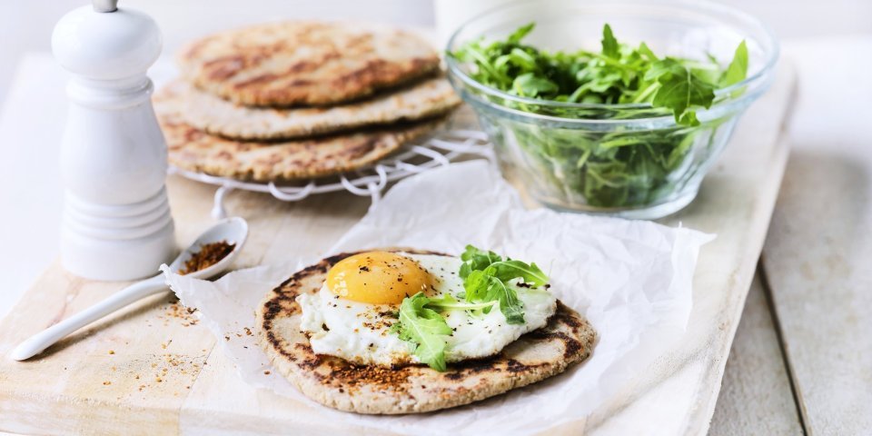 Het yoghurtbrood ligt op een houten snijplank. Hierop liggen meerdere ingrediënten om aan de slag mee te gaan, denk maar aan rucola, peper, extra yoghurt. 