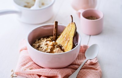 Een lichtroos ontbijtkommetje staat op tafel, met hierin de kruidige chai porridge met een halve peer en een kaneelstokje. Er is ook een roze theepot met bijpassend kopje.