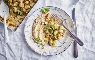 Op tafel staat de ovenschaal met geroosterde spruitjes, hiernaast staat een bord gevuld met een schep van de bonenspread en bovenop al enkele geroosterde spruitjes. 