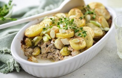 Een ovenschotel staat op het midden van de tafel, er is al een portie uitgeschept. Je ziet het gehakt onderaan liggen, met spruitjes , stukjes knolselder en goudgele aardappelschijfjes. 