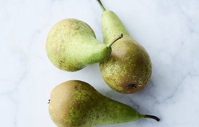 Drie peren liggen op een marmere aanrecht. De kleuren van de conference peren zijn groen en komen mooi uit op het werkblad van witte marmer.