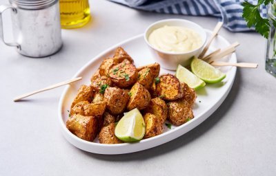 In een ovaal wit bord liggen de stukjes aardappel goudkrokant gebakken uit de airfryer. Er staat een dipsausje bij met enkele partjes limoen. We gebruiken houten vorkprikkertjes om de aardappel op te prikken en te dippen in het sausje. 