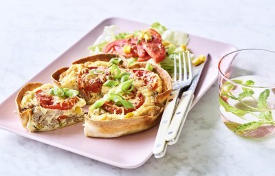 Een klaargemaakte quiche ligt op een roze en rechthoekig bord klaar om te eten. De quichebodem bestaat uit een wrap met hierin het quichebeslag en de groenten. 