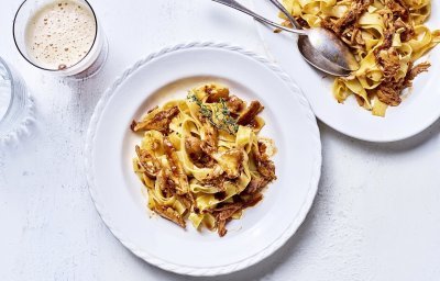 Op tafel staat een wit bord gevuld met tagliatelle en konijnenragout. Er staat een biertje langs, aangezien de ragout gemaakt is met Belgisch bier. 