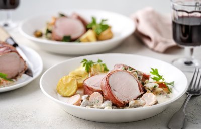 Op tafel staan twee porties uitgeschept. Het heerlijk bereide varkenshaasje ligt op de romige champignonsaus met plakjes wortel. Er liggen ook ovengeroosterde aardappeltjes bij. Langs het bord ligt een servette, glaasje rode wijn en bestek. 