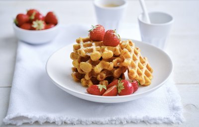 Op een bordje liggen enkele wafels met verse aardbeien en wat bloemsuiker. Er staat ook nog een tasje koffie langs. 