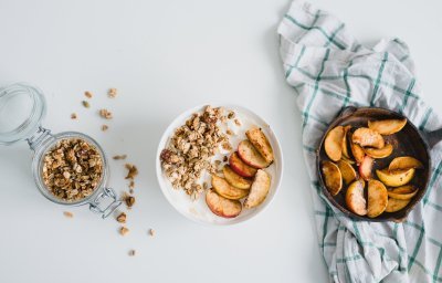 Op tafel staat een ontbijtkommetje gevuld met yoghurt, granola en lauwwarme appeltjes. 