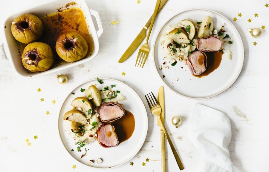 Feestelijk hoofdgerecht van varkenshaasje met een puree van aardpeer en ovenappeltjes. Goud bestek en gouden minikerstballetjes liggen langs het bord en geeft instant een Kerslook.