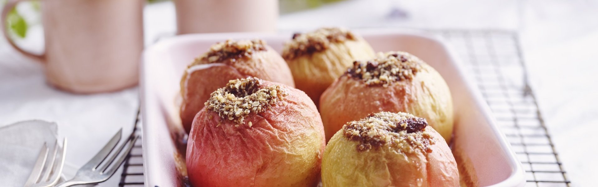 Gevulde appels in een licht roze ovenschaal. Achteraan staan twee roze kopjes, klaar om aan het ontbijt te beginnen.