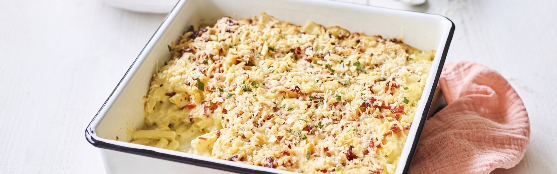 Een heerlijke gevulde ovenschotel boordevol comfortfood staat op de tafel te blinken. Onze mac and cheese met Belgische kazen zit in een witte ovenschotel met donker blauw randje, zoals bij de bomma. Er ligt een zalmroze servette langs en de een takje verse peterselie voor extra kleur in het beeld. 