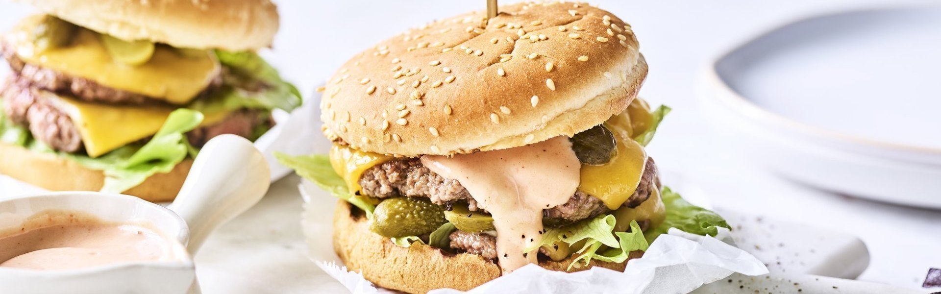 Twee heerlijke burgers liggen klaar op een marmere snijplank. Het vlees is verdeeld in twee dunne porties met de saus en gesmolten kaas er bovenop. De burgers worden recht gehouden door middel van een prikker.