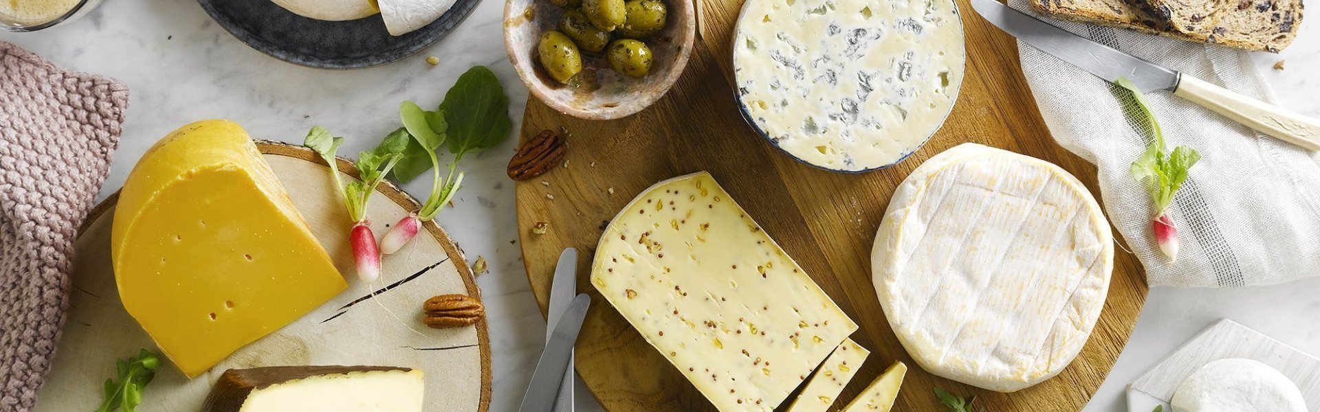 Kaasschotel op marmeren keukenblad. Verschillende Belgische kazen liggen op houten planken met brood, noten, radijzen en chutney erbij. 